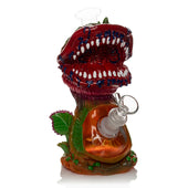 Lit Silicone 9" Venus Fly Trap Water Pipe .
A novelty glass water pipe shaped like a red dinosaur mouth with white teeth, green leaves, and an amber-colored glass body, shown on a white background.