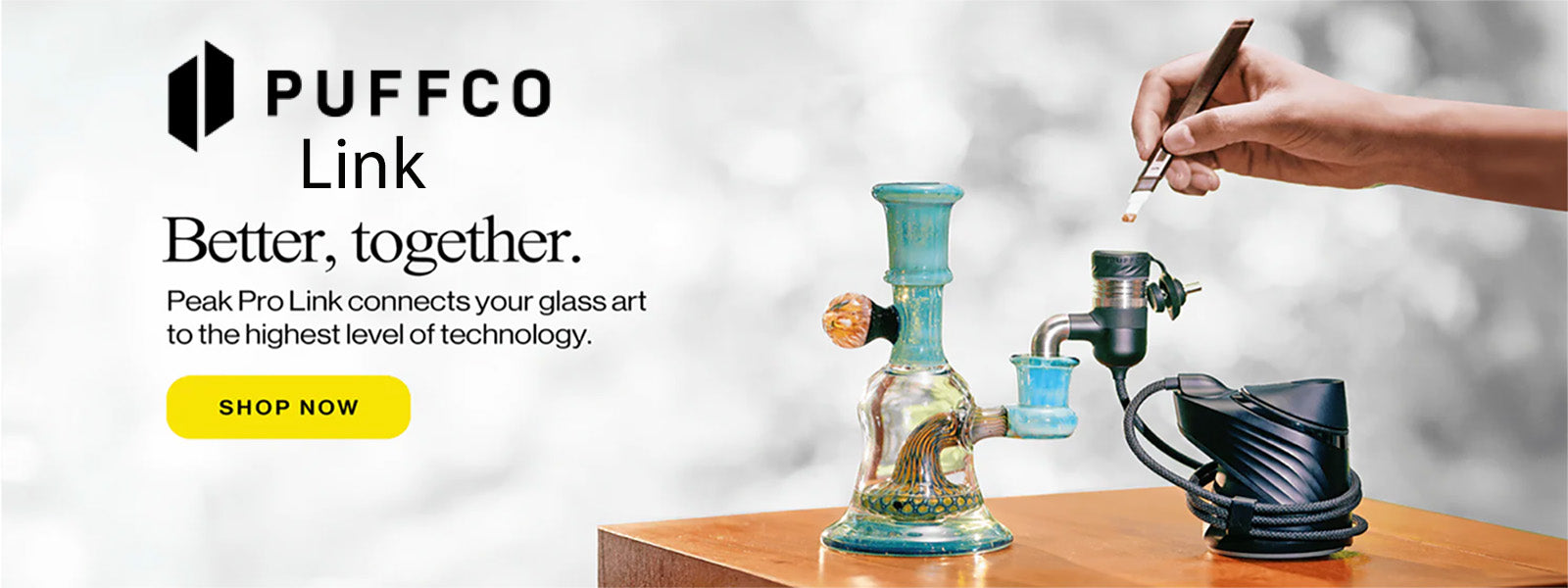 Puffco Link device with a hand interacting with it on a wooden surface, against a light gray background.